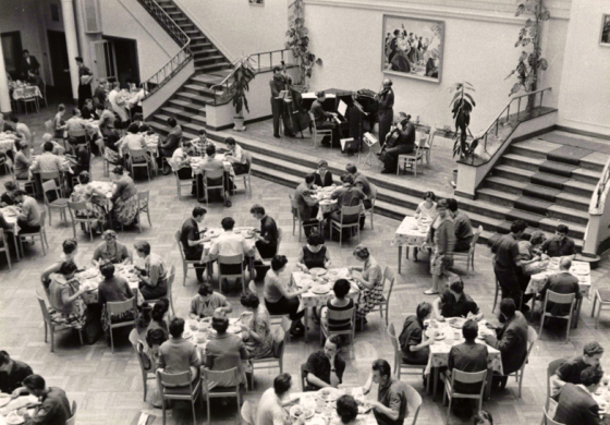 Menschen an Tischen vor Kulturhausbühne der FDJ-Schule am Bogensee